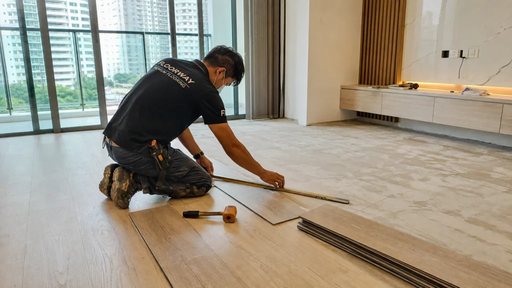 SPC Flooring Installation Singapore – Professional Floor Installer at Work Professional floor installer installing SPC flooring in a modern Singapore apartment using measuring tools and preparing the floor surface during a home renovation.